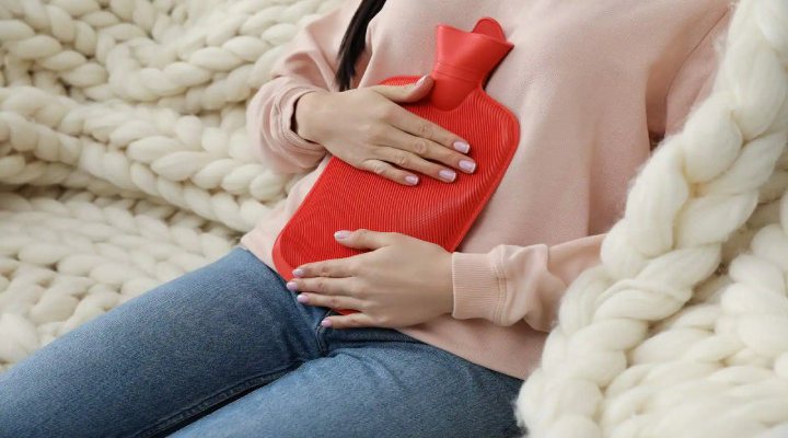 گذاشتن کیسه آب گرم روی شکم برای درمان خانگی منوراژی